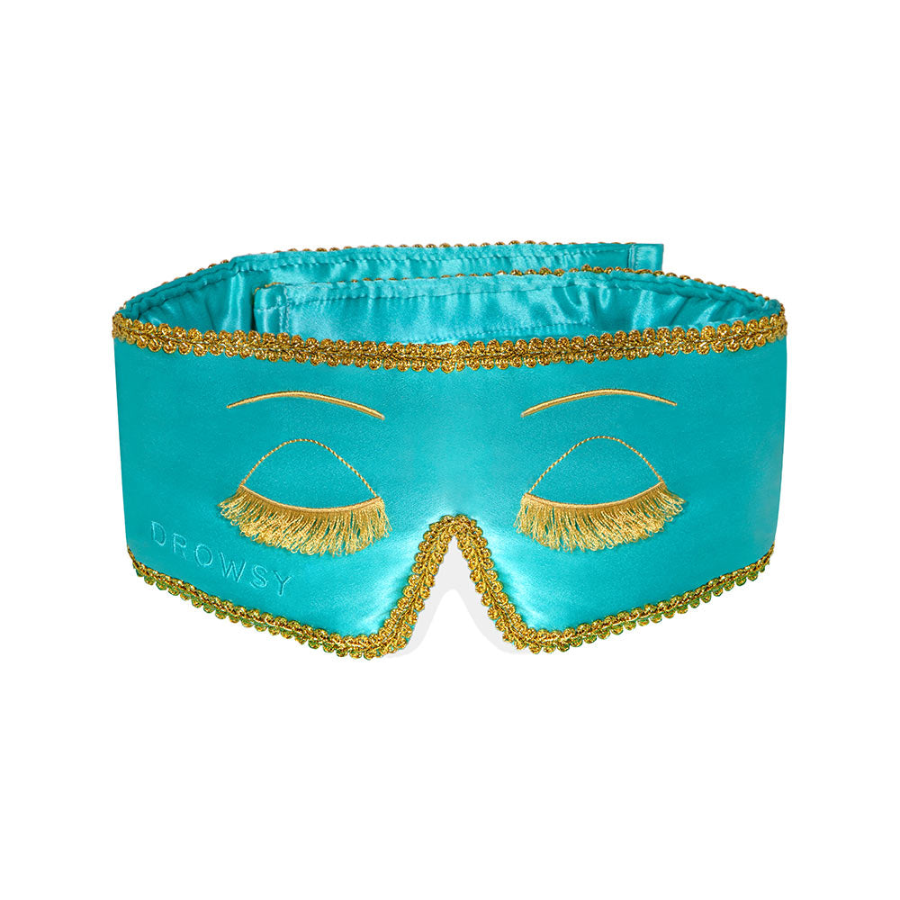 The Breakfast at Drowsy mask features turquoise mulberry satin silk, gold fringe eyelashes, gold trim, and DROWSY embroidery. Its blackout design ensures a comfortable, restful fit for luxurious sleep.