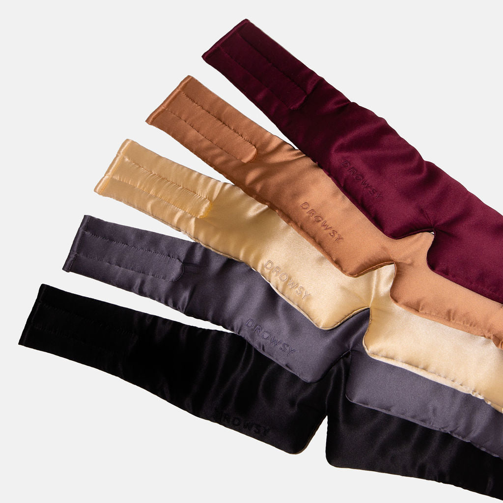 The Family Pack includes five padded silk sleep masks in burgundy, bronze, gold, black, and gray, displayed in a fanned-out pattern on a white background.