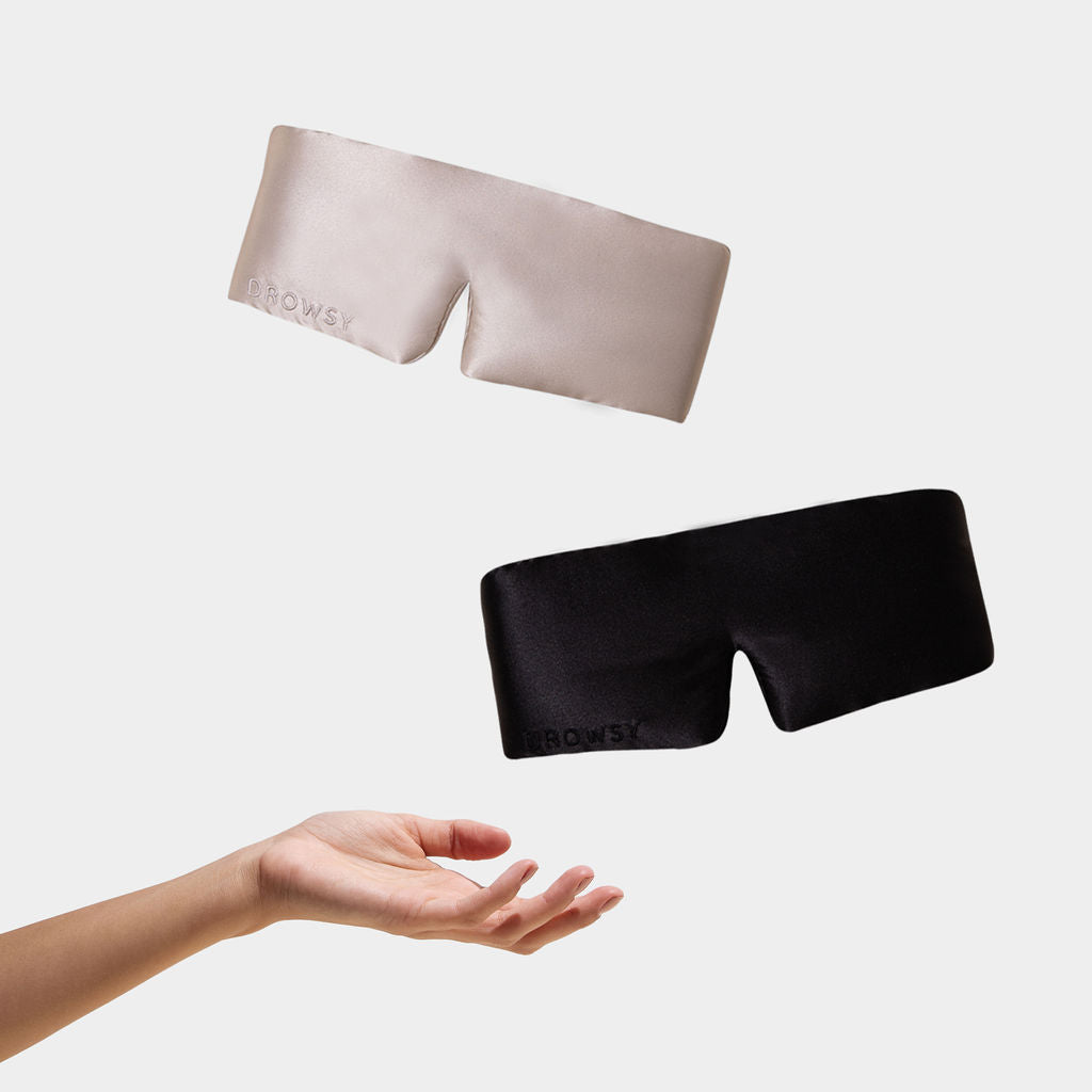 A hand tosses two curved eye masks from the Lovers Pack—one beige, one black—each with "BROWSEY" embroidered on the corner, against a plain white background.