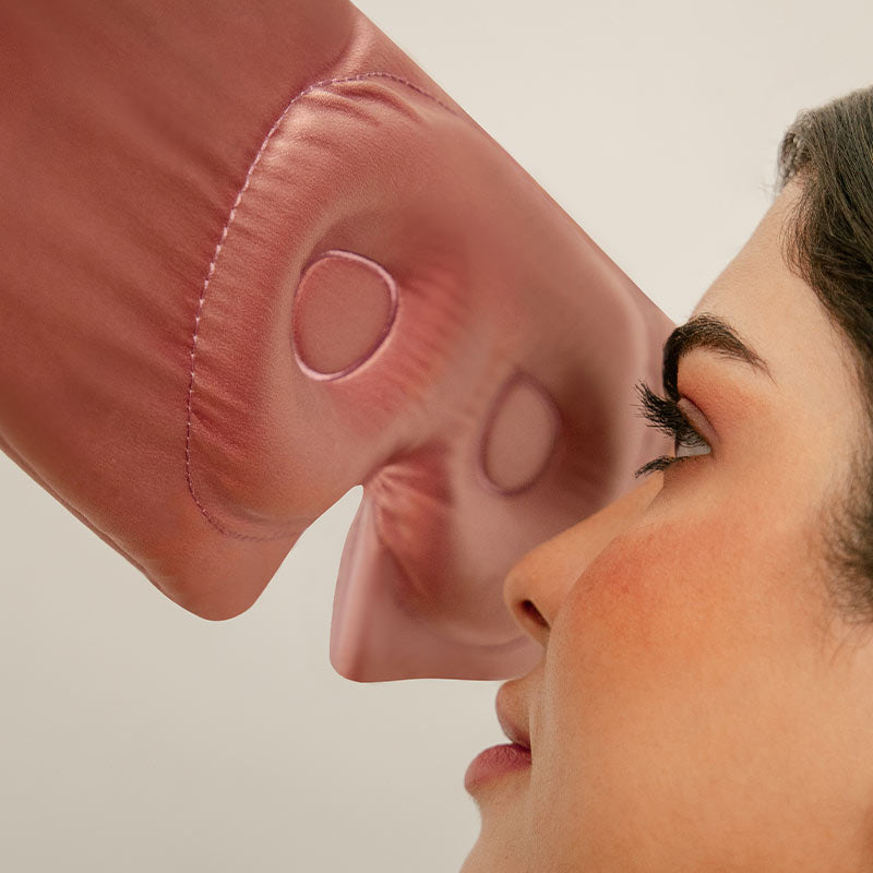A close-up of a womans face in profile, with a pink, shiny boxing glove gently pressing against her nose, creating an indentation. The background is plain and light-colored.