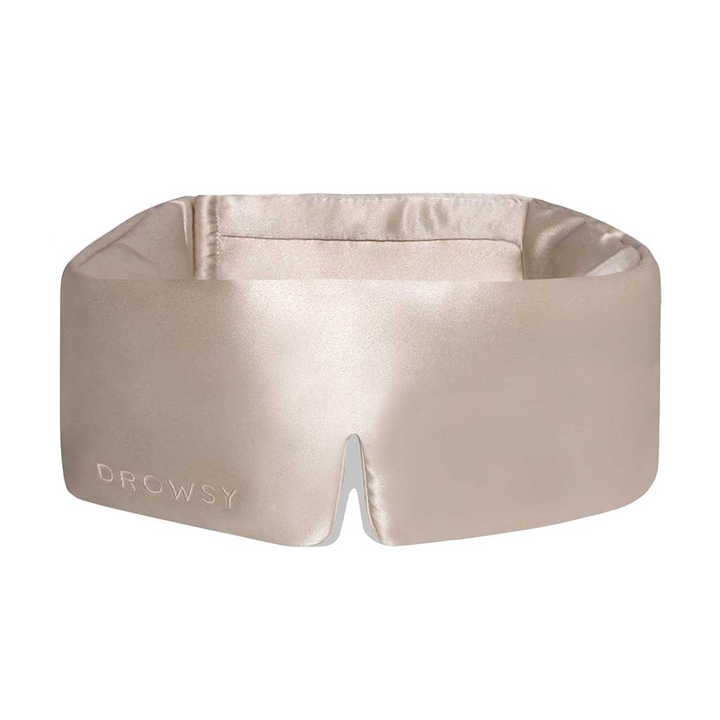 The Dusty Gold silk eye mask features a soft, padded design, full blackout coverage, a bottom-center notch for comfort, and “DROWSY” embroidered on the left side—perfect for ultimate beauty sleep.
