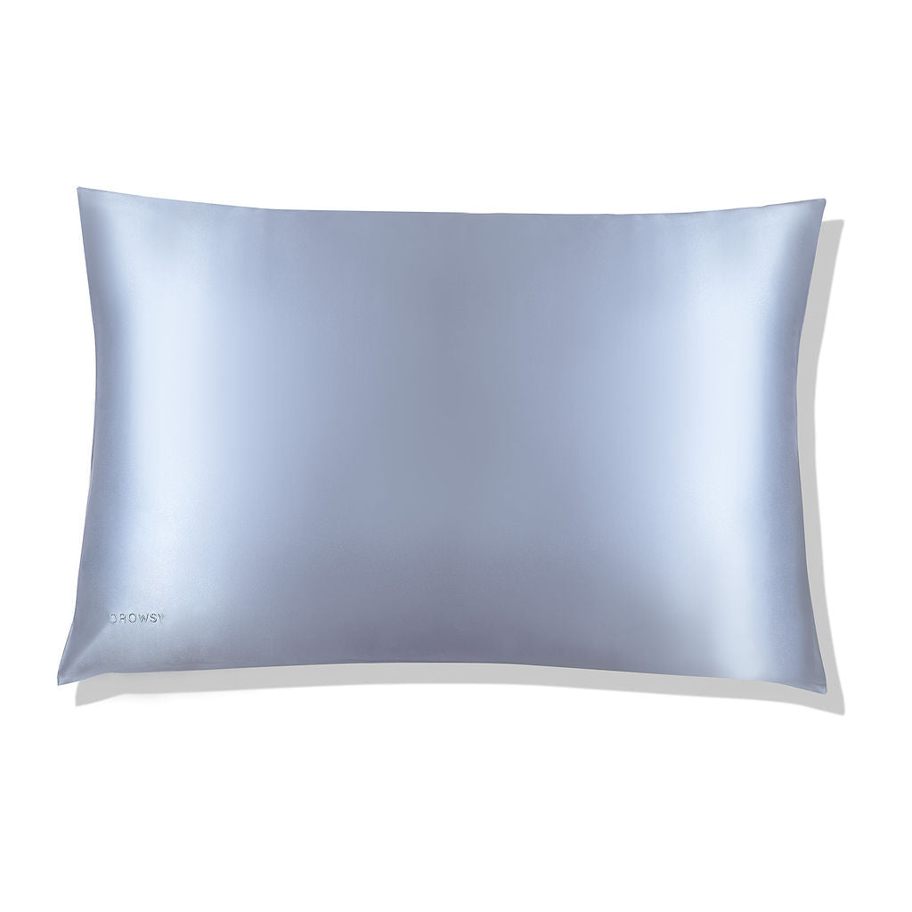 The Blue Belle Silk Pillowcase, in smooth light blue silk with a subtle sheen, lies flat on a white background. DROWSY is printed on the bottom left—ideal for hair protection and beauty routines.