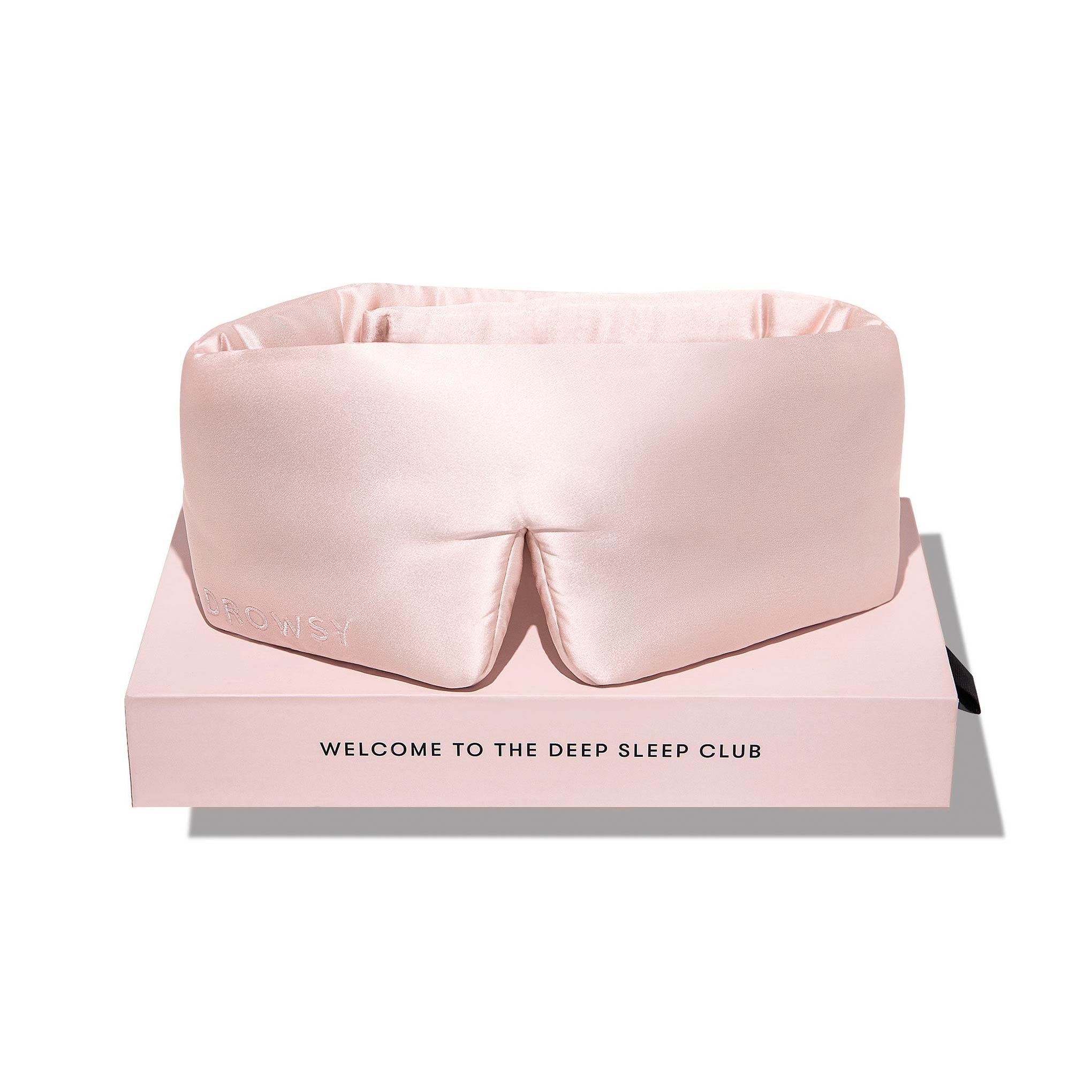 The Sunset Pink silk eye mask, embossed with DROWSY, rests on a matching pink box reading WELCOME TO THE DEEP SLEEP CLUB—your ticket to beauty sleep and fewer dark circles.