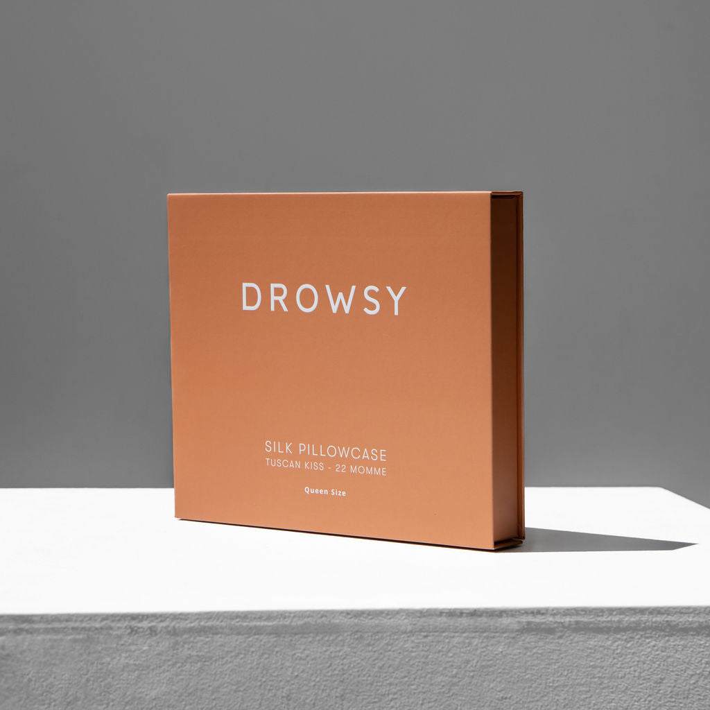 A rectangular, peach-colored box labeled Pumpkin Spice Silk Pillowcase stands upright on a white surface against a gray background—this hair-protecting beauty essential features Tuscan Kiss, 22 Momme silk, and Queen Size.