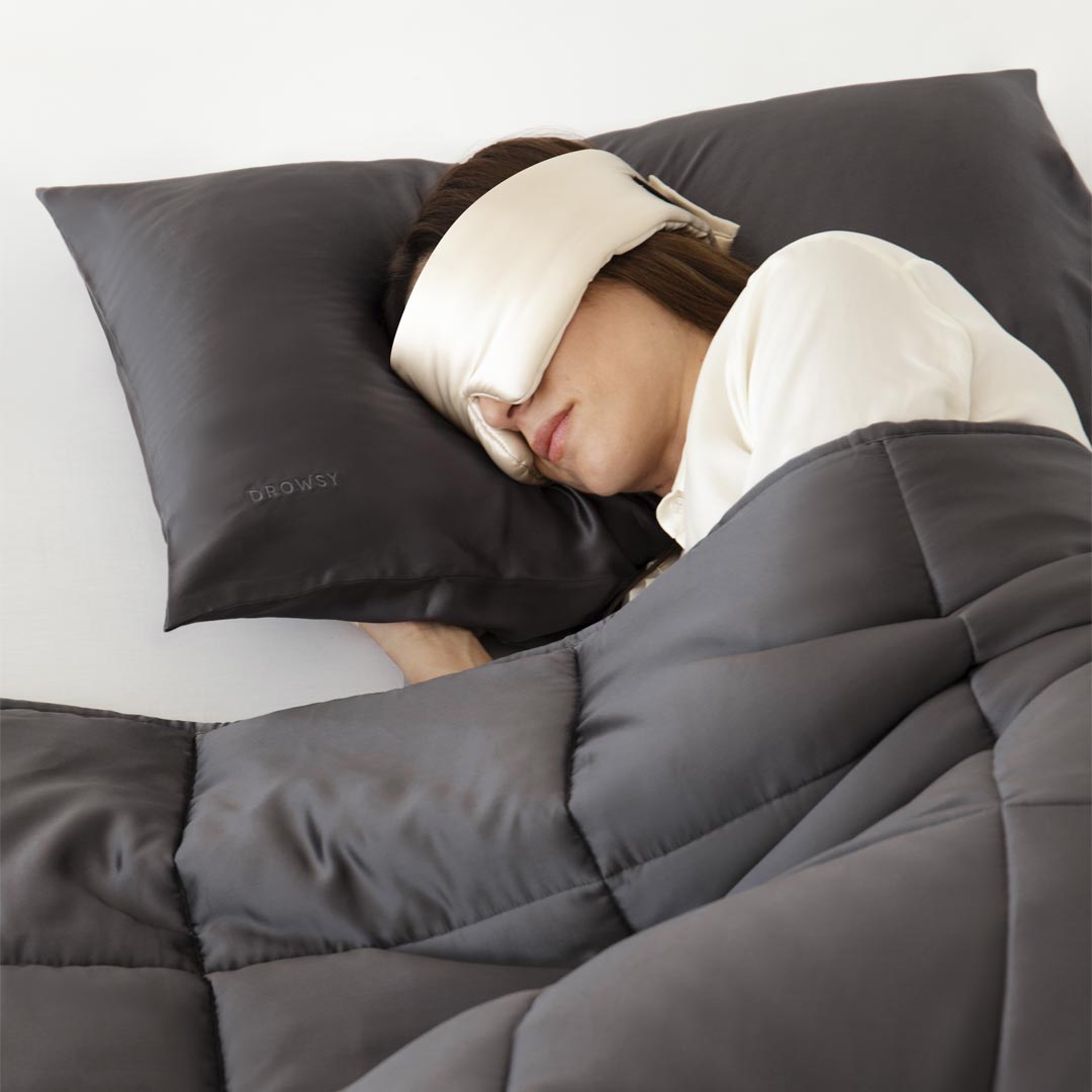A person appears to be peacefully asleep, lying on a gray pillow and covered with the Moonlight Shadow Silk Weighted Blanket.
