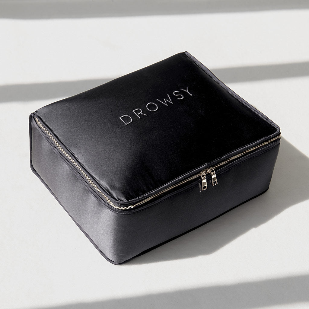 A black, rectangular zippered pouch with “DROWSY” in white letters rests on a light surface with diagonal shadows—ideal for storing your Moonlight Shadow Silk Weighted Blanket and enjoying deep relaxation.