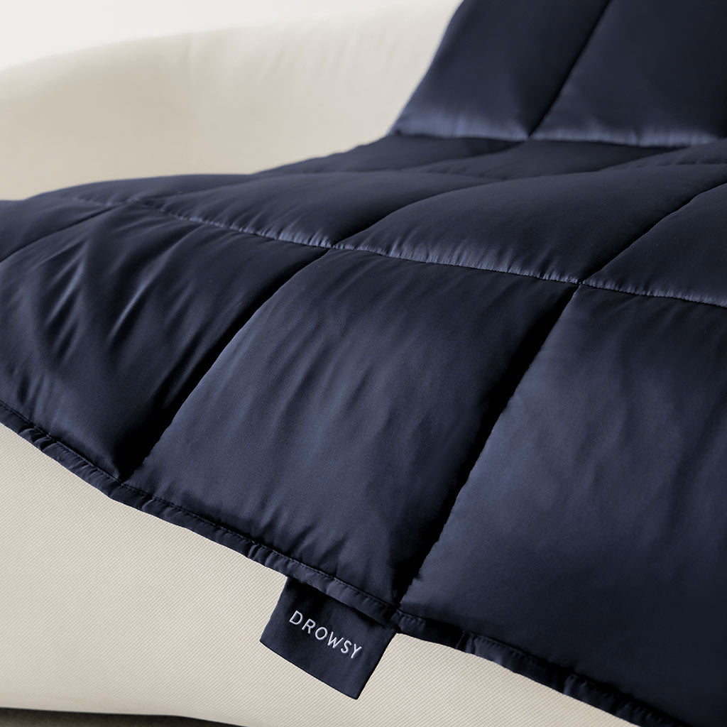 The Midnight Blue Silk Weighted Blanket is draped over a light cream sofa. Its smooth, slightly shiny finish enhances the inviting look, making it perfect for deep relaxation.