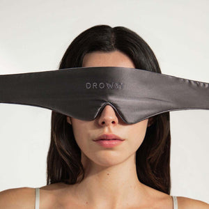 A woman wears the Moonlight Shadow Featherweight Sleep Mask, a wide black silk mask covering her eyes and nose for a complete blackout experience, against a plain white background.