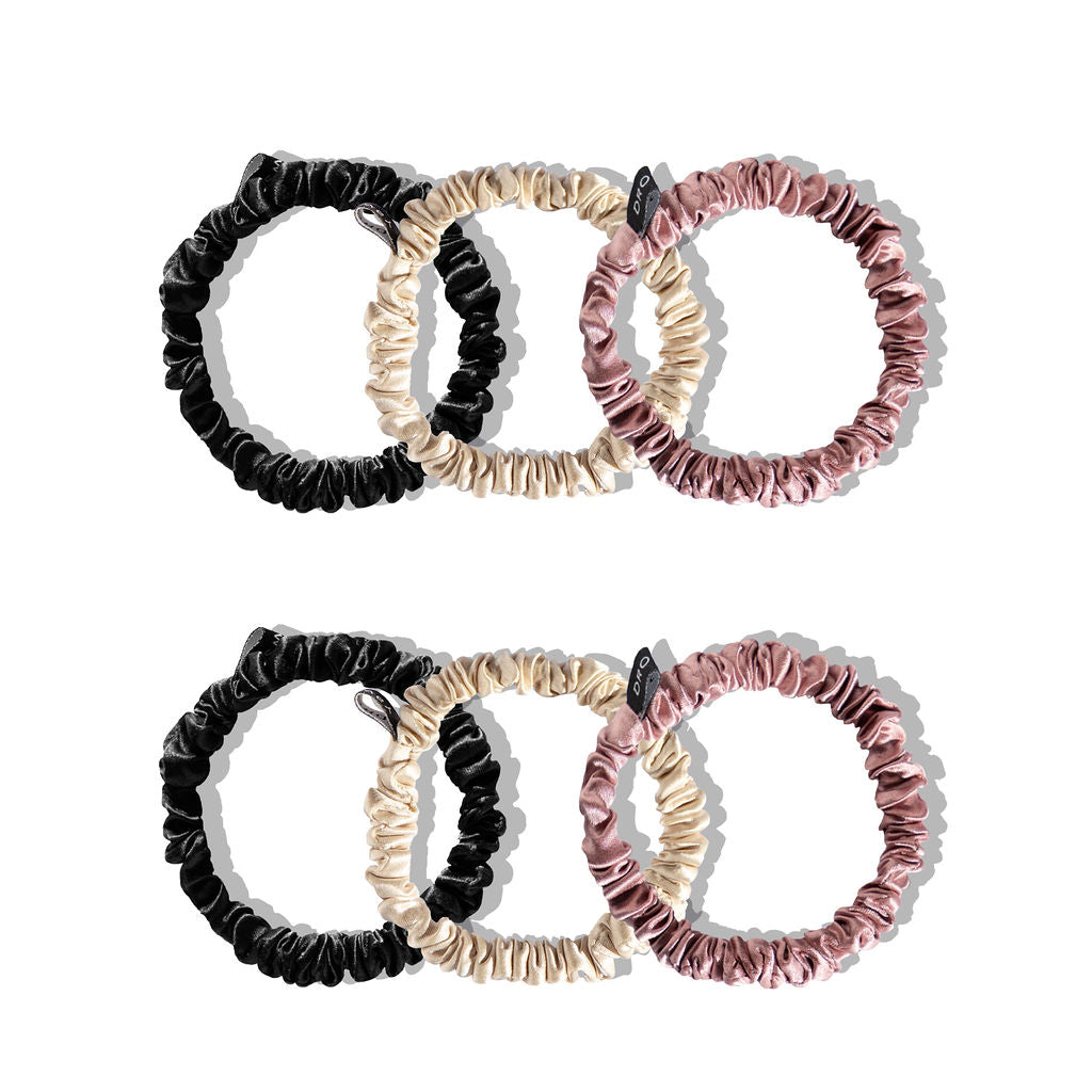 Six silk scrunchies in black, beige, and mauve, arranged in two rows of three on a white background.