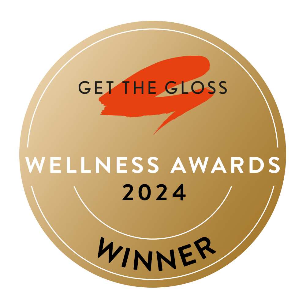 A gold circular badge with a red brushstroke and the text GET THE GLOSS WELLNESS AWARDS 2024 WINNER in white and black, enclosed in a gold square border.