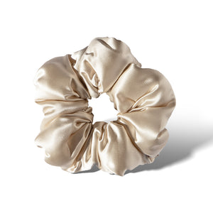 The Dusty Gold - Padded Scrunchie features soft, shiny beige satin gathered around an elastic band to add hair volume, displayed against a white background with a subtle shadow on the right.