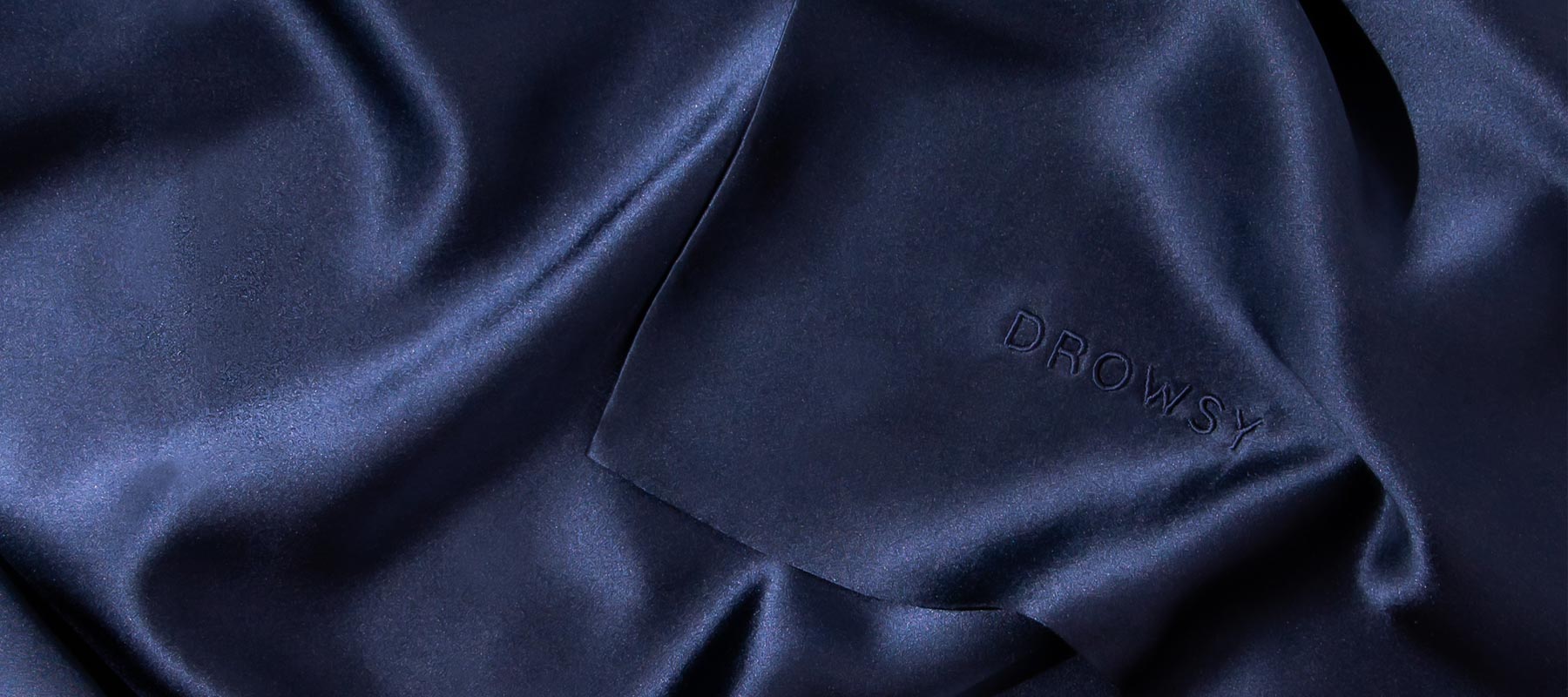 Smooth, dark navy blue silk fabric with subtle sheen and the word DROWSY embroidered discreetly in matching thread on one corner.