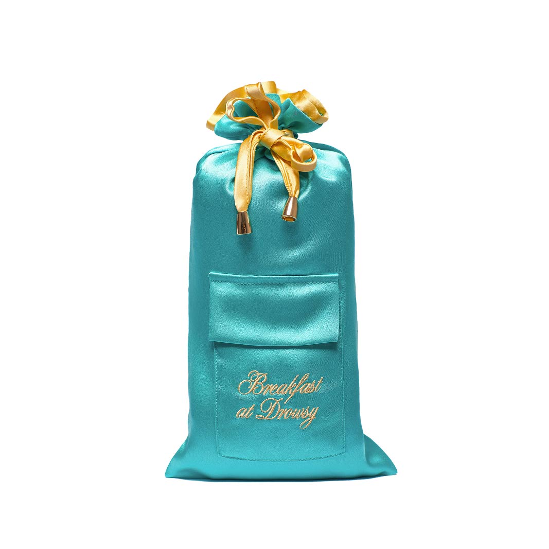 The drowsysleepco Breakfast at Drowsy Turquoise Carry Pouch is a silk drawstring bag with a yellow ribbon, front pocket, and gold "Breakfast at Drusy" embroidery—ideal for storing your sleep mask. Photographed against a white background.