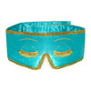 A woman with long brown hair and a relaxed expression leans against a white wall, wearing the Breakfast at Drowsy turquoise silk sleep mask with gold trim and tassel eyelash details pushed up on her forehead.