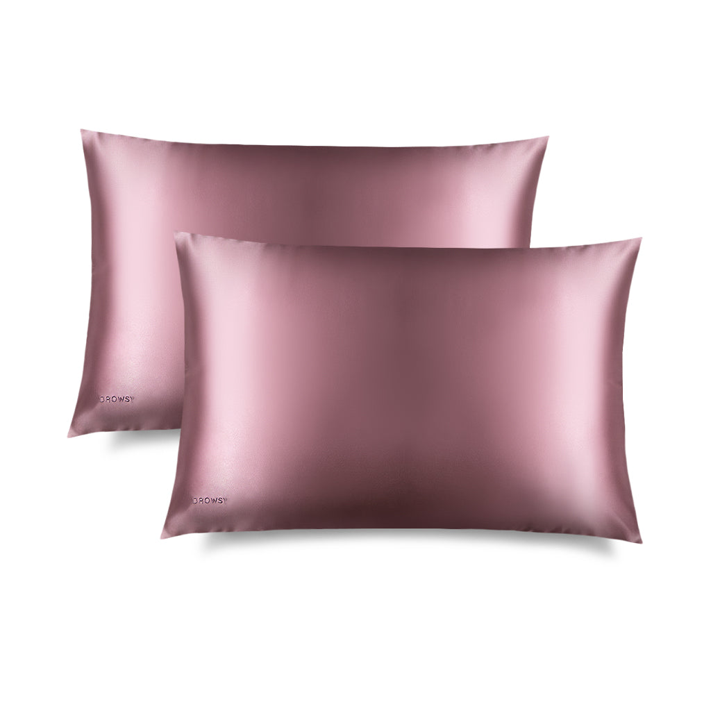 Two Damask Rose Silk Pillowcases feature a sleek pink rectangular design with a subtle embroidered DROWSY logo in the lower left corner, displayed on a white background with a soft right shadow—an essential for hair protection and skincare.