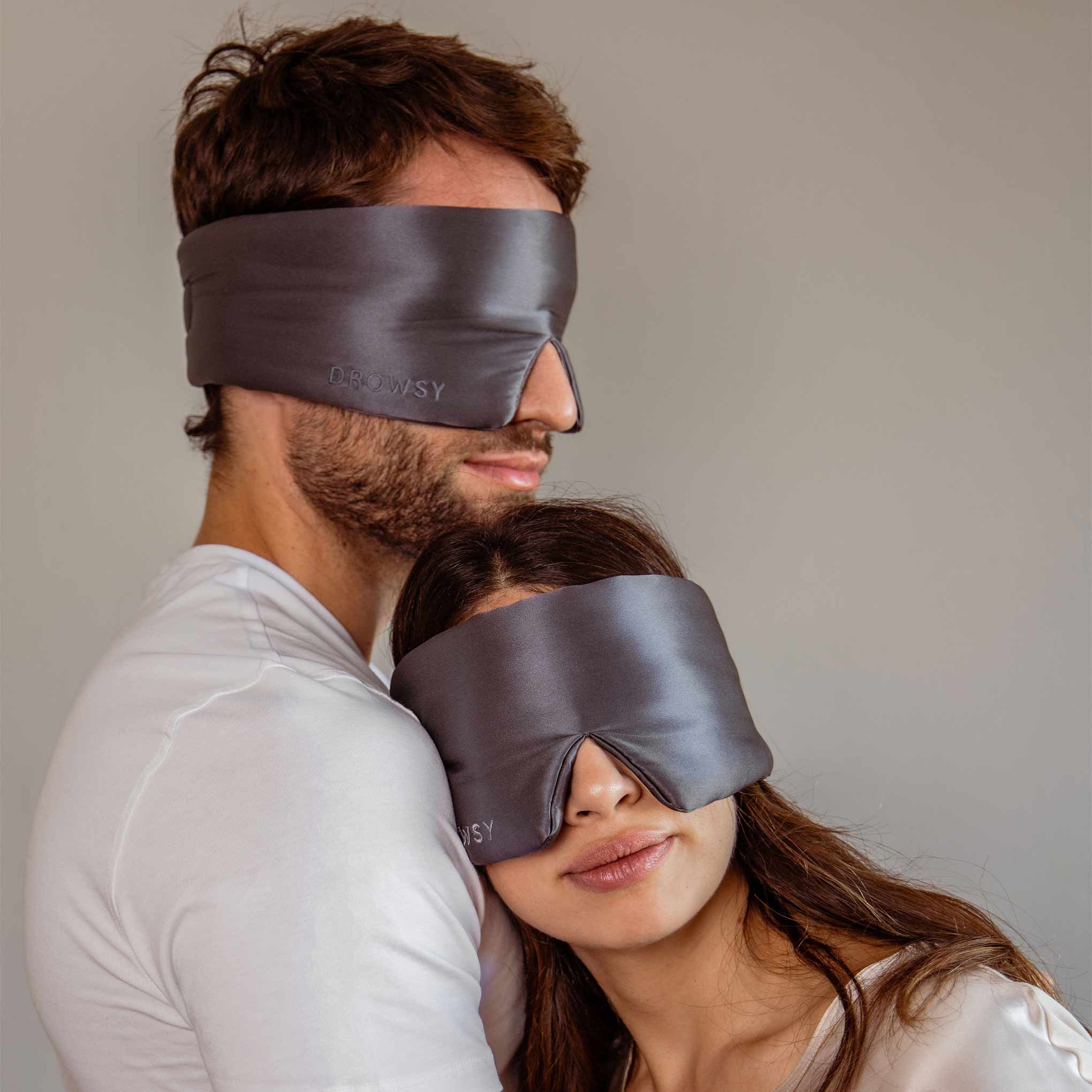 Male and female model hugging with grey silk sleep masks covering their eyes