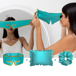 A woman in a white camisole stands before a mirror, holding the drowsysleepco Hollywood Experience bundle—Original: a turquoise silk sleep mask, matching pillowcase, and scrunchie with gold trim—luxurious essentials for ultimate beauty sleep.