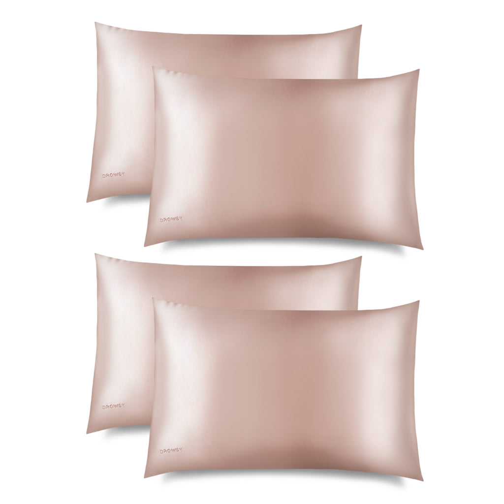 Four Sunset Pink Silk Pillowcases with a smooth, shiny finish are stacked and slightly overlapping on a white background. Each hair-protecting pillowcase has the word "DROWSY" subtly embroidered in the corner.