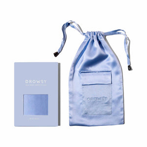 A light blue satin drawstring pouch, the Blue Belle Silk Carry Pouch with a pocket and DROWSY embossed, is shown next to its matching light blue box labeled DROWSY Silk Mask Carry Pouch on a white background.