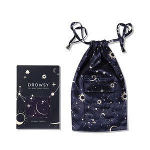 A dark blue silk sleep mask and mulberry silk pouch with a star and moon pattern, beside a matching box labeled Cosmic Energy Silk Carry Pouch.