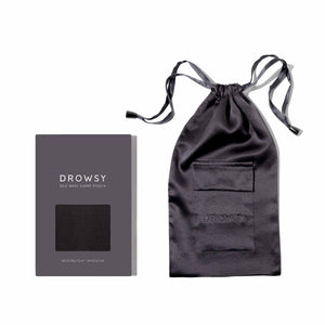 A black Moonlight Shadow Silk Carry Pouch with a pocket and drawstring rests beside a gray box labeled Drowsy Silk Mask Caddy Pouch.