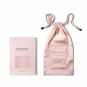 The Sunset Pink Silk Carry Pouch, made from pale pink mulberry silk with a pocket, is shown beside its matching packaging—ideal for storing your favorite silk sleep mask in style.