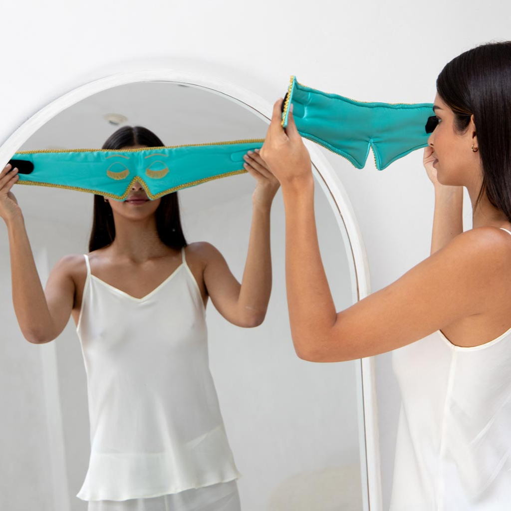 A woman wearing a white camisole stands before a mirror, holding the Perfect Skin Bundle 