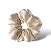 The Dusty Gold - Padded Scrunchie features soft, shiny beige satin gathered around an elastic band to add hair volume, displayed against a white background with a subtle shadow on the right.