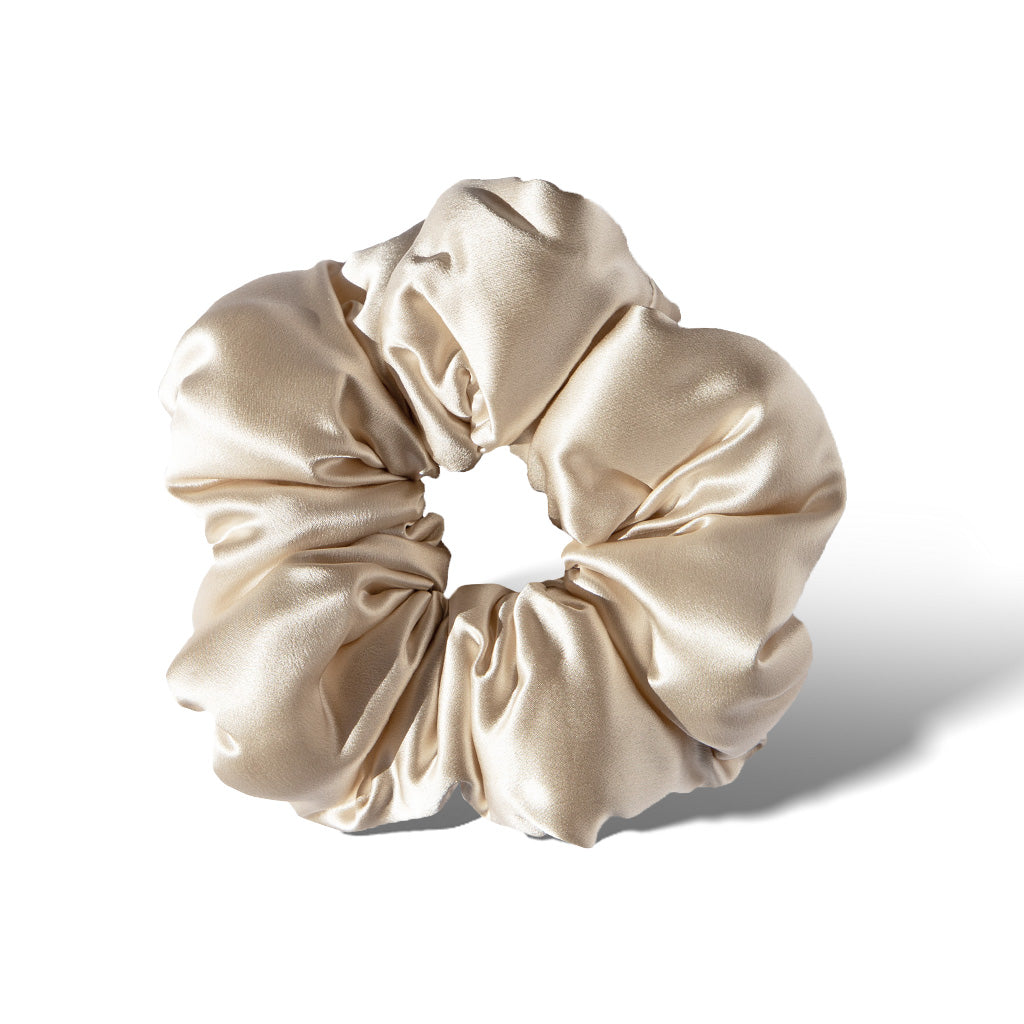 The Dusty Gold - Padded Scrunchie features soft, shiny beige satin gathered around an elastic band to add hair volume, displayed against a white background with a subtle shadow on the right.