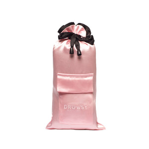 The Sleep and the City Silk Carry Pouch by drowsysleepco is a pink satin drawstring bag with a black ribbon, front pocket, and DROWSY embroidery—an elegant, luxury sleep mask pouch standing upright against a white background.