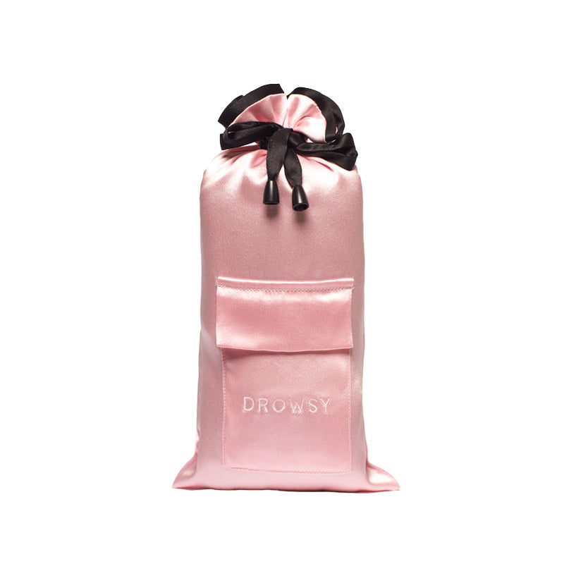 The Sleep and the City Silk Carry Pouch by drowsysleepco is a pink satin drawstring bag with a black ribbon, front pocket, and DROWSY embroidery—an elegant, luxury sleep mask pouch standing upright against a white background.