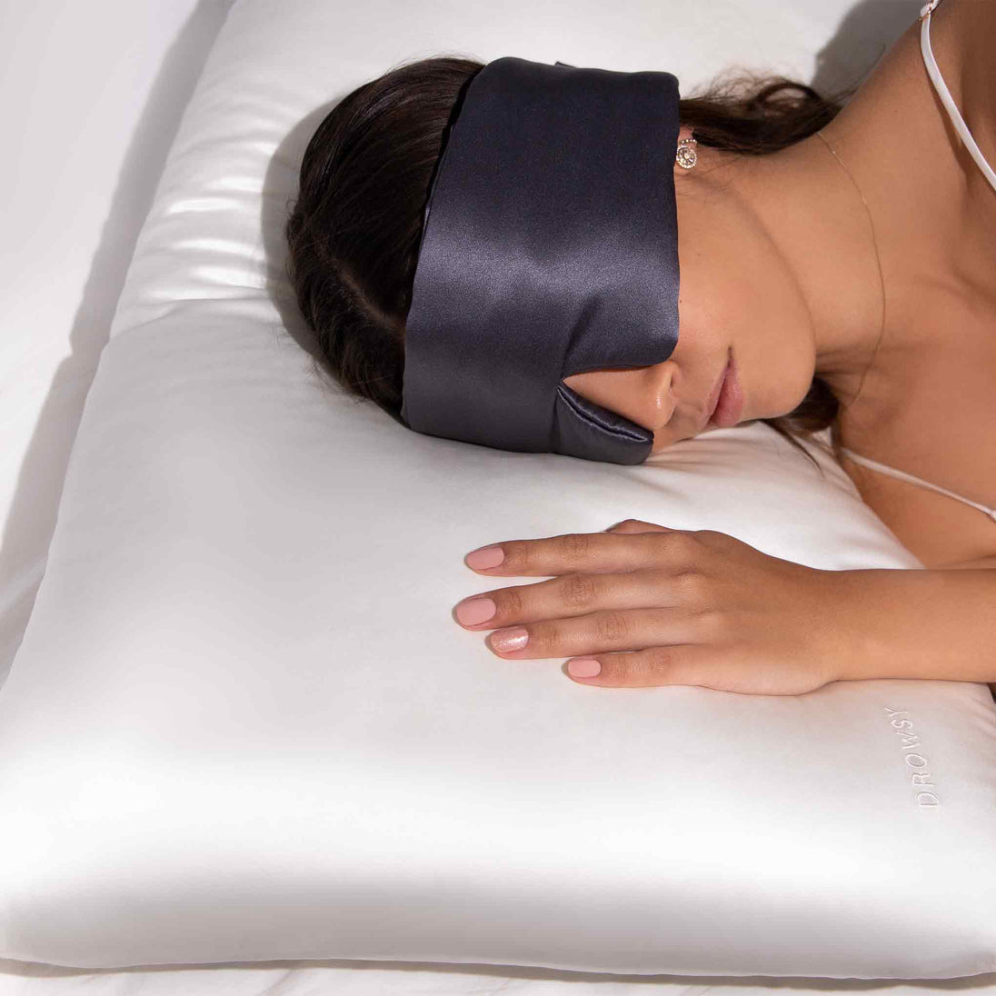 Girl sleeping on white silk pillow case with Drowsy Sleep co grey sleep mask covering her eyes
